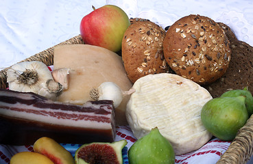 Image showing Rustic still life of bread, cheese, bacon and figs in a wicker basket