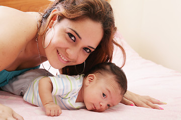 Image showing Hispanic mom lying down on bed and holding her infant son