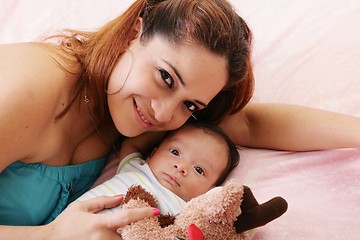 Image showing Happy mum and baby boy smiling in the bed holding teddy bear