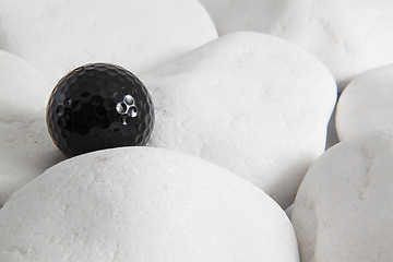 Image showing Black golf ball and white stones