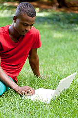 Image showing young smiling african student sitting in grass with notebook