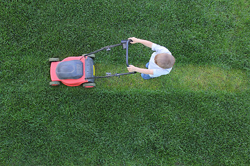 Image showing Little boy cuts a grass using lawn-mower