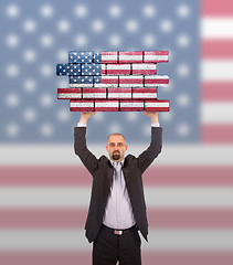 Image showing Businessman holding a large piece of a brick wall