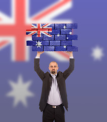 Image showing Businessman holding a large piece of a brick wall