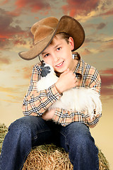 Image showing Farm boy sitting on bale of hay holding a chicken