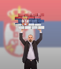 Image showing Businessman holding a large piece of a brick wall