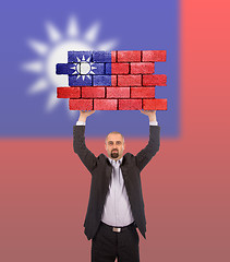 Image showing Businessman holding a large piece of a brick wall