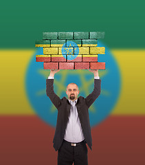 Image showing Businessman holding a large piece of a brick wall