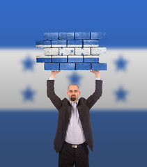 Image showing Businessman holding a large piece of a brick wall