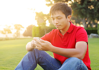 Image showing man sits on grass and use mobile phone