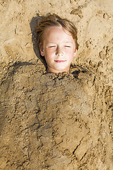 Image showing happy boy dig oneself in the sand