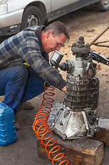 Image showing A man cleans the engine taken from the car for overhaul , withou