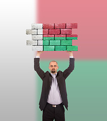 Image showing Businessman holding a large piece of a brick wall