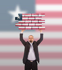 Image showing Businessman holding a large piece of a brick wall