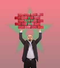 Image showing Businessman holding a large piece of a brick wall