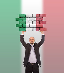 Image showing Businessman holding a large piece of a brick wall