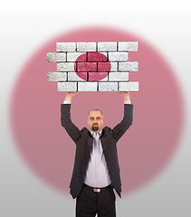 Image showing Businessman holding a large piece of a brick wall