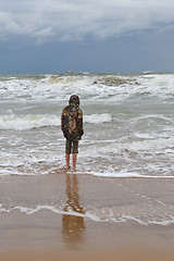 Image showing The teenager costs on the seashore in a jacket and barefoot. 