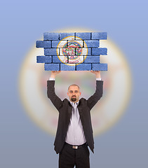 Image showing Businessman holding a large piece of a brick wall