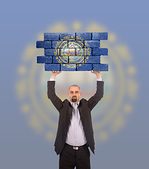 Image showing Businessman holding a large piece of a brick wall