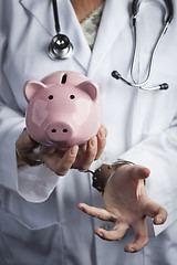 Image showing Doctor In Handcuffs Holding Piggy Bank Wearing Lab Coat, Stethos