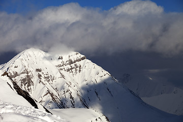 Image showing Snowy sunlit mountains and blue sky with clouds