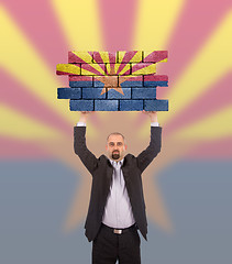 Image showing Businessman holding a large piece of a brick wall