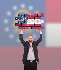 Image showing Businessman holding a large piece of a brick wall