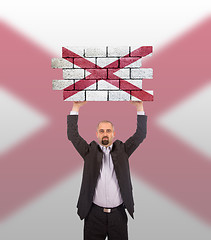 Image showing Businessman holding a large piece of a brick wall