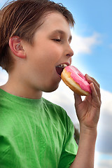 Image showing Boy biting a yummy pink iced doughnut (donut)