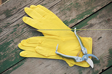 Image showing Yellow rubber gloves and garden pruner on wooden background.