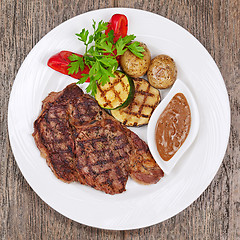 Image showing Grilled steaks, baked potatoes and vegetables on white plate on 