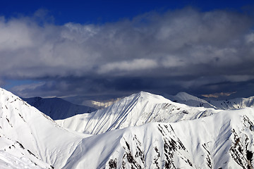 Image showing Snowy sunlit mountains and cloudy sky