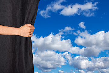 Image showing Hand opening black curtain with sky behind it