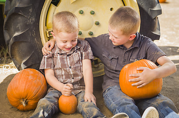 Image showing Two Boys Holding Pumpkins Talking and Sitting Against Tractor Ti
