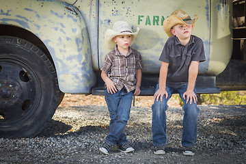 Image showing Two Young Boys Wearing Cowboy Hats Leaning Against Antique Truck