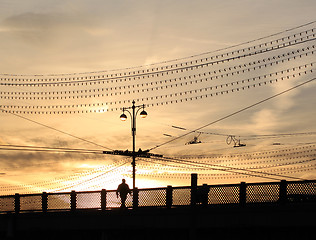 Image showing A man walks across the bridge at sunset