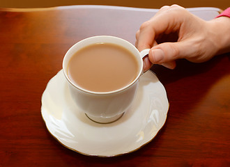 Image showing Woman picking up a cup of tea from a table