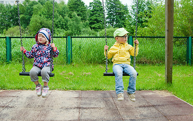 Image showing Young children, a boy with a girl swinging on a swing