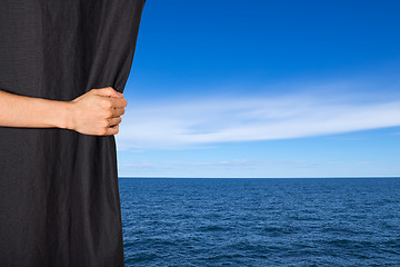 Image showing Hand opening black curtain with sea and sky behind it