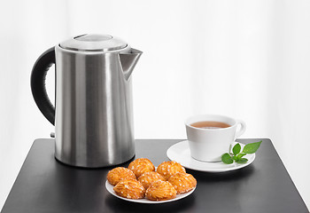 Image showing Electric kettle, cup of tea and cookies on a table
