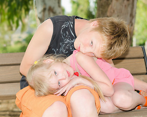 Image showing Brother and sister curled up together on the bench in park