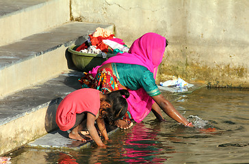 Image showing Indian woman with daughter washing clothes in lake