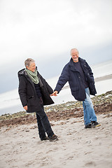 Image showing mature happy couple walking on beach in autumn