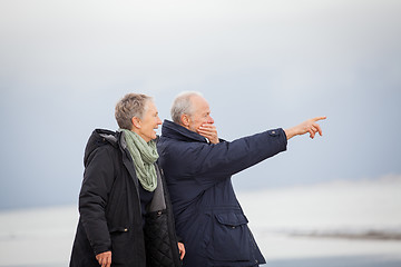 Image showing mature happy couple walking on beach in autumn