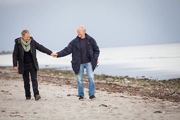 Image showing mature happy couple walking on beach in autumn