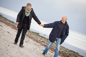 Image showing mature happy couple walking on beach in autumn