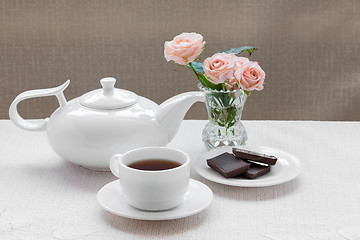 Image showing teapot, cup, roses, and chocolate on a plate