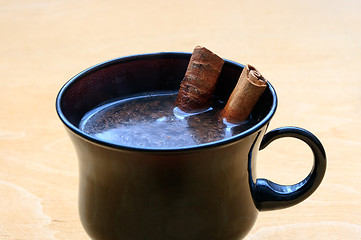 Image showing Cup of coffee with cinnamon sticks on wooden table