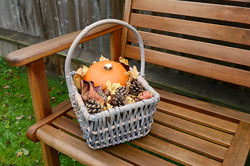 Image showing Basket with pumpkin, leaves and fir cones on a bench